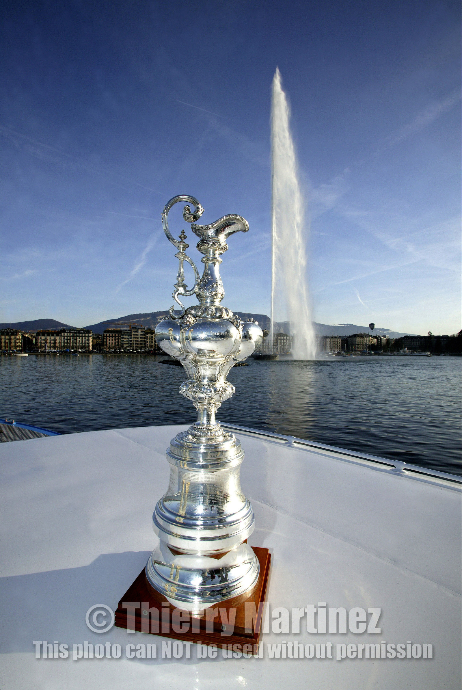 03_2291D ©Th.Martinez .Geneva , Switzerland. America's Cup 2003. 9th March 2003.Alinghi Team winner of America's Cup 2003..The America's Cup on the way to her new home, La Societe Nautique de Geneve (which is Alinghi Yacht Club). Alinghi Team and the CUP did a short trip by the Lac to arrive at La Nautique. On the way stop for a photo The Cup with jet deaude Geneve in the backgroung.